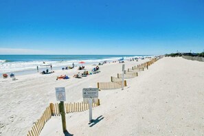 Ein Strand mit Holzzaun, Sonnenschirmen und entspannten Personen.