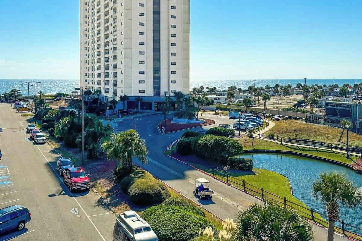 A high-rise hotel with a parking lot, a golf cart, and a body of water.