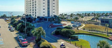 A high-rise hotel with a parking lot, a golf cart, and a body of water.