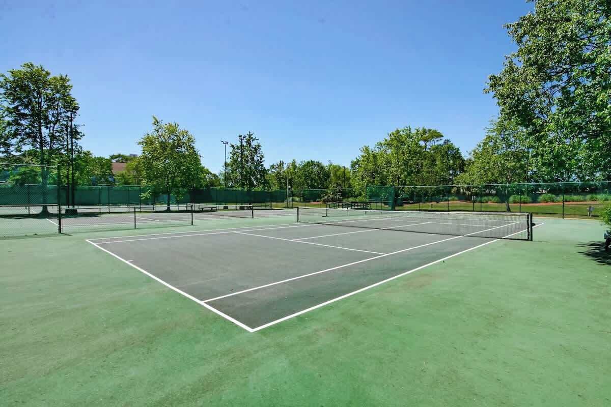 Una cancha de tenis con red, rodeada de árboles y una cerca.
