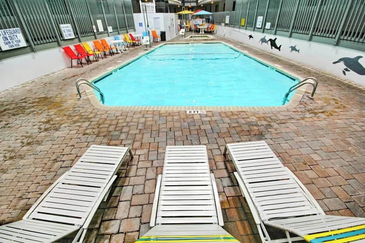 An indoor swimming pool with a tiled floor, multiple lounge chairs, and a lifeguard on duty sign.