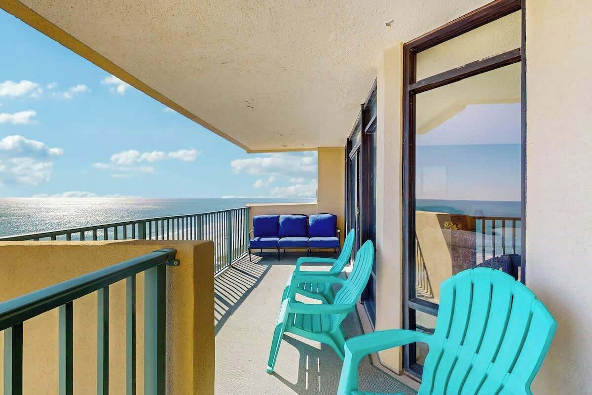 Un balcon avec vue sur la mer, deux chaises bleues et une table.