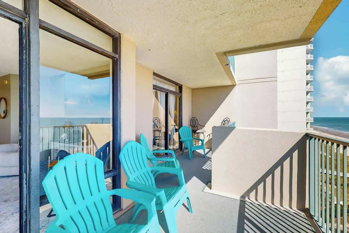 Un balcon avec des chaises turquoise et une table, donnant sur une plage.