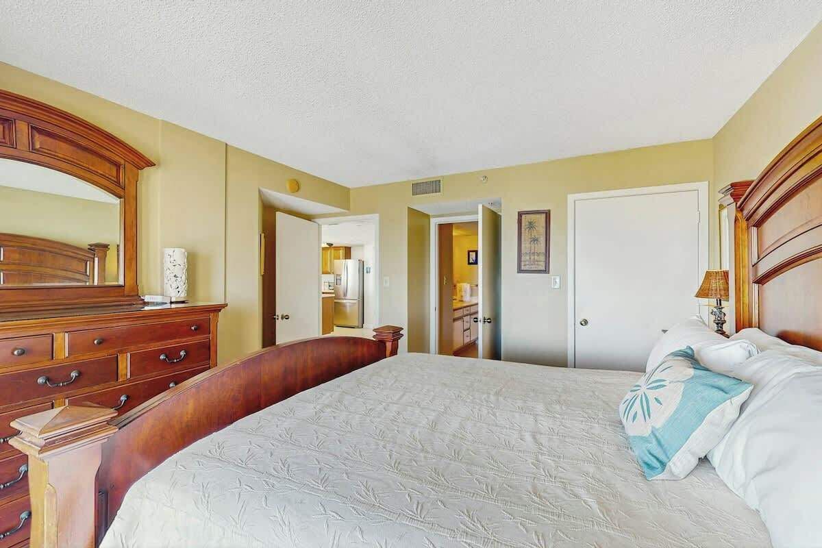A hotel room with a large bed, wooden dresser, and a mirror.