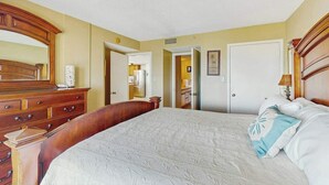 Quarto de hotel com uma cama grande, cómoda de madeira e espelho.