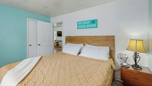 Um quarto com cama, mesa de cabeceira, luminária e um aviso na parede.