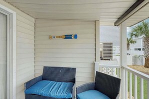 Eine überdachte Veranda mit zwei Korbstühlen und einem blauen Kissen.