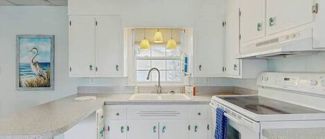 A kitchen with white cabinets, a sink, a stove, and pendant lights.