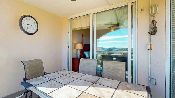 A balcony with a table and chairs, a clock on the wall, and a view of the city. - North Tower Unit 301 (North Myrtle Beach)