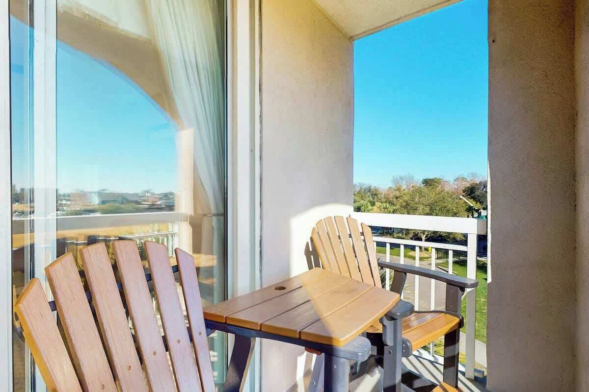 A balcony with a wooden table and chairs, a view of the cityscape, and a white railing.