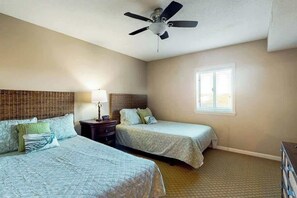 Ein Schlafzimmer mit zwei Betten, einem Deckenventilator, einem Fenster und einem Nachttisch mit Lampe.