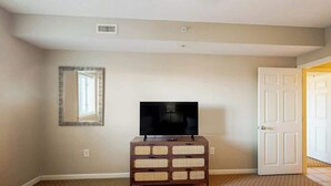 A hotel room with a television on a wooden dresser, a door, and a patterned carpet. - North Tower Unit 301 (North Myrtle Beach)