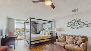 A modern bedroom with a four-poster bed, a sofa, a coffee table, and a view of the outdoors. - Yacht Club Villas 2-304 (North Myrtle Beach)