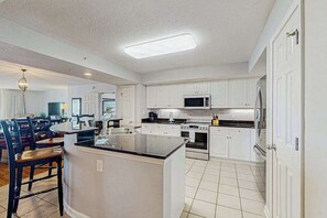 Una cocina moderna con armarios blancos, una isla central y un comedor con sillas.