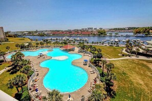 Une grande piscine à plusieurs niveaux, entourée d’une terrasse et dotée de chaises longues, le tout offrant une vue imprenable sur un port de plaisance et le paysage urbain.