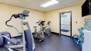 Et fitnesscenter med træningsmaskiner, en vandautomat og et fjernsyn monteret på væggen.