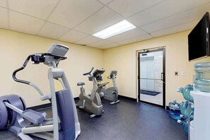 Ein Fitnessraum mit Cardiogeräten, einem Wasserspender und einem an der Wand montierten Fernseher.