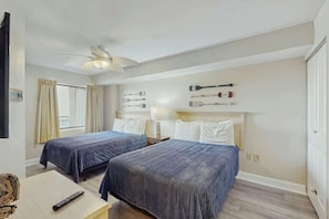 A hotel room with two beds, a ceiling fan, a window with curtains, and a wall-mounted lamp. - Sand Dunes Resort 1609 (Myrtle Beach)