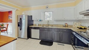 A kitchen with white cabinets, a stainless steel refrigerator, a dishwasher, and a granite countertop. - Lighthouse Retreat at the Beach (Myrtle Beach)