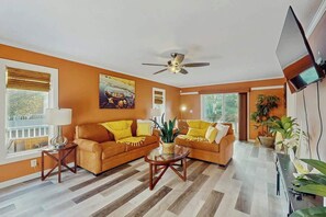 Ein Wohnzimmer mit zwei Sofas, einem Couchtisch, einem Deckenventilator und einem an der Wand befestigten Fernseher.