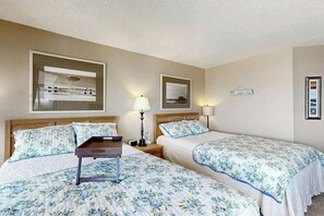 Ein Hotelzimmer mit zwei Betten, einem Nachttisch, einer Lampe und einem gerahmten Bild an der Wand.