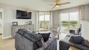 A living room with a sofa, a dining table, and a television mounted on the wall. - Tilghman Beach and Golf 1519 (North Myrtle Beach)