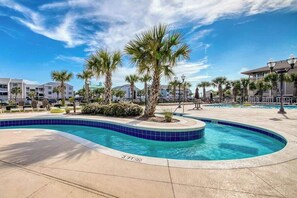 Ein Swimmingpool mit blauer Fliesenbordüre, Palmen und blauem Himmel.