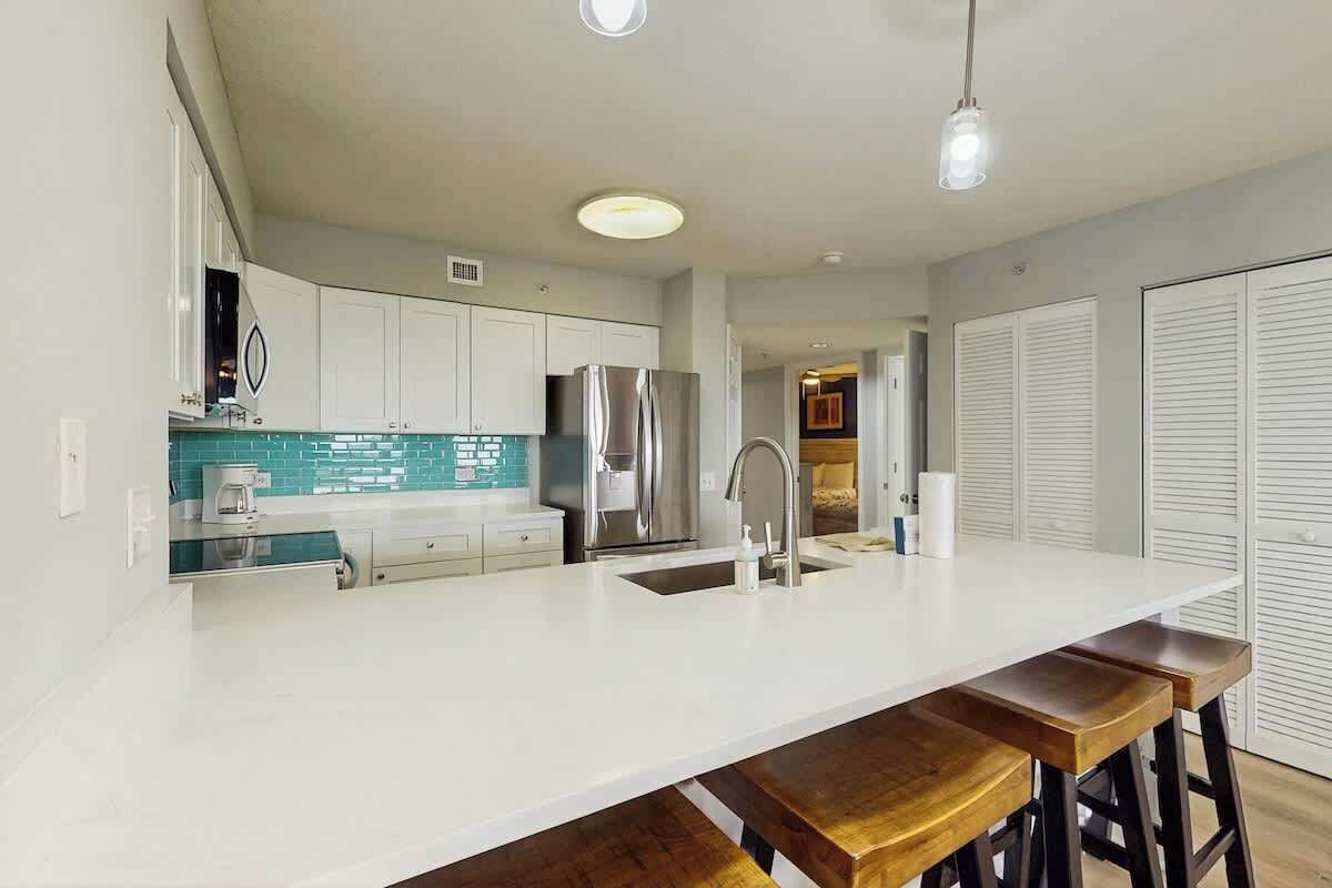 A modern kitchen with white cabinets, a stainless steel refrigerator, and a bar stool area.