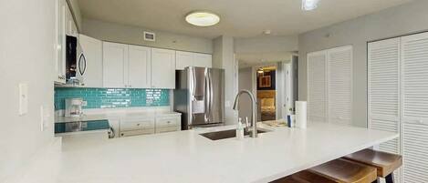 A modern kitchen with white cabinets, a stainless steel refrigerator, and a bar stool area.