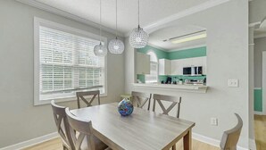 Uma área de refeições com mesa e cadeiras, um vaso e uma cozinha ao fundo.