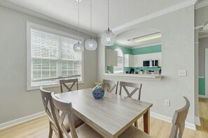 Ein Essbereich mit Tisch und Stühlen, einer Vase sowie einer Küche im Hintergrund.