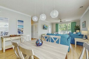 A modern living room with a dining area, a blue sofa set, and a decorative vase on the table. - River Crossing at Barefoot 125 (North Myrtle Beach)
