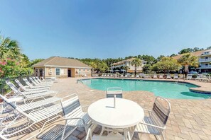 Ein Poolbereich mit Liegestühlen und einem Tisch, umgeben von Gebäuden und Palmen.