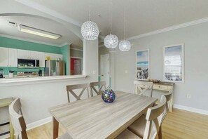 A dining area with a wooden table and chairs, a decorative globe, pendant lights, and a kitchen in the background. - River Crossing at Barefoot 125 (North Myrtle Beach)