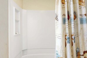 A bathroom with a white bathtub, a shower curtain with bird and nature patterns, and a small shelf unit. - Renaissance Tower 317 (Myrtle Beach)