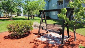 A wooden swing set in a landscaped area with a red mulch bed and a small bush. - Renaissance Tower 317 (Myrtle Beach)