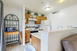 A compact kitchen with a microwave, stove, and refrigerator. There is a wooden cabinet with a plant on top and a small sink area. - Renaissance Tower 317 (Myrtle Beach)