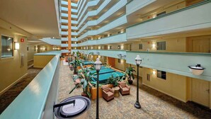 En hotellobby med flere etager, et centralt siddeområde med stole og borde, samt en swimmingpool.