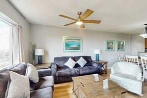 A living room with a dark grey sofa, a patterned armchair, a wooden coffee table, and a ceiling fan. - Tilghman Beach and Golf 6003 (North Myrtle Beach)