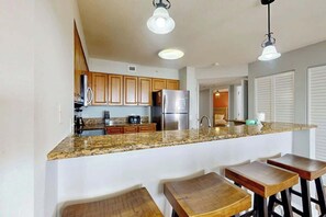 A kitchen with granite countertops, wooden cabinets, stainless steel appliances, and bar stools. - Tilghman Beach and Golf 6003 (North Myrtle Beach)