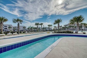 Piscina com borda em azulejo azul, cercada por palmeiras e edifícios.