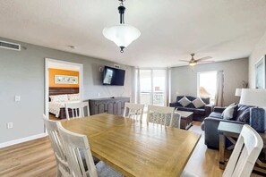 A spacious living area with a dining table, chairs, a sofa, a TV, and a ceiling fan. - Tilghman Beach and Golf 6003 (North Myrtle Beach)