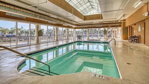 En indendørs swimmingpool med glasvægge, et ovenlys og udsigt til palmer udefra.
