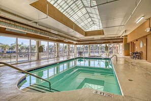 An indoor swimming pool with clear glass walls, a skylight, and a view of palm trees outside. - Tilghman Beach and Golf 6003 (North Myrtle Beach)
