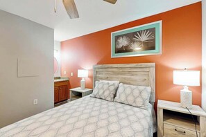 A bedroom with a bed, two bedside tables with lamps, a wooden headboard, and a wall-mounted picture. - Tilghman Beach and Golf 6003 (North Myrtle Beach)
