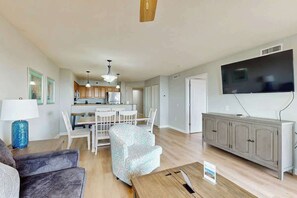 A modern living room with a sofa, a patterned armchair, a wooden coffee table, and a TV mounted on the wall. - Tilghman Beach and Golf 6003 (North Myrtle Beach)
