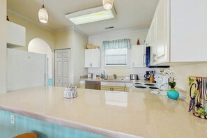 A kitchen with white cabinets, a central island, and a window with a curtain. - Wild Iris Unit 303 Condo (Myrtle Beach)