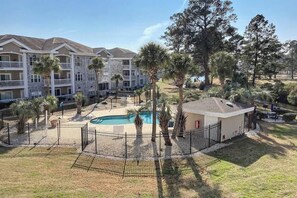 A multi-story hotel with a swimming pool, surrounded by palm trees and a fenced courtyard. - Wild Iris Unit 303 Condo (Myrtle Beach)