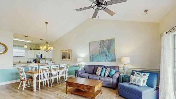 Ein Wohnzimmer mit Esstisch, Stühlen, einer Couch, einem Couchtisch und Deckenventilator.
