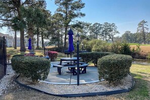 A landscaped outdoor area with a circular arrangement of picnic tables and benches, surrounded by trimmed hedges and a lamp post. - Wild Iris Unit 303 Condo (Myrtle Beach)